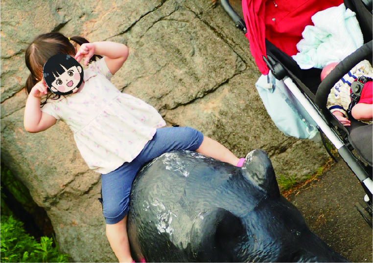 園内にあるクマの石像にまたがってポーズをとる女の子と、その横にあるベビーカーで眠る赤ちゃんの様子。