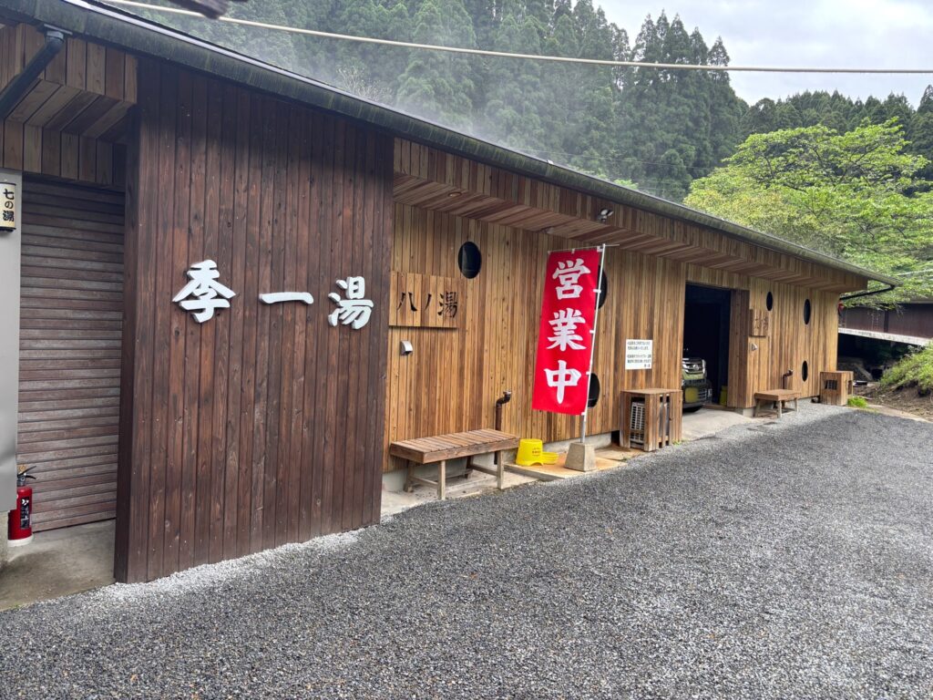 霧島の家族風呂「季一湯」の外観。木目調の壁に「季一湯」と書かれた看板と「営業中」の赤い旗、個室の入り口が並ぶ様子。