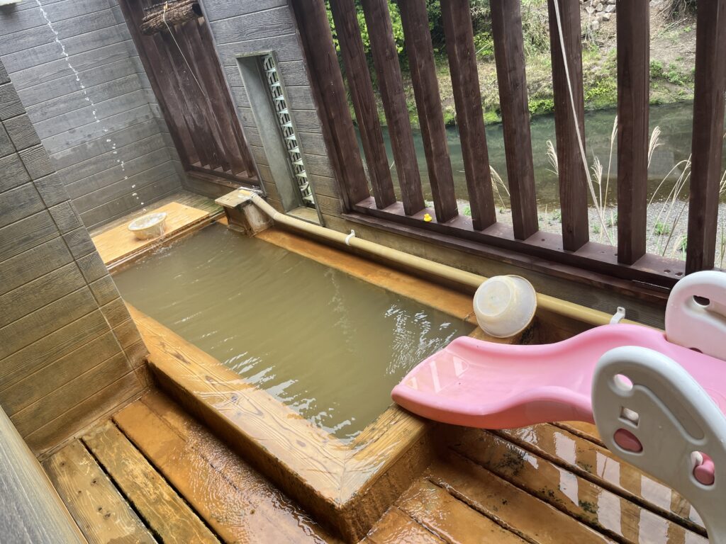 季一湯「九ノ湯」の露天風呂。すぐ横を流れる川のせせらぎや霧島の自然を間近に感じられる開放的なロケーション。浴槽には子供用のピンクの滑り台が設置されており、親子で楽しめる造り。